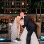 Groom dips and kisses bride in front of fountain